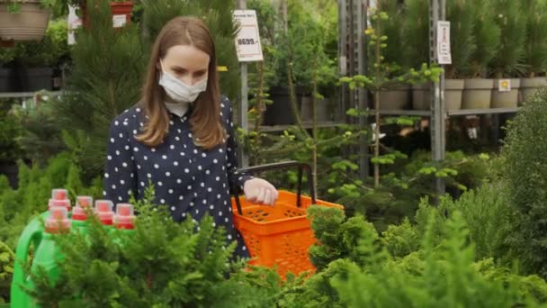 Mujer con una cesta elige plantas para comprar para su jardín en una tienda de plantas — Vídeos de Stock