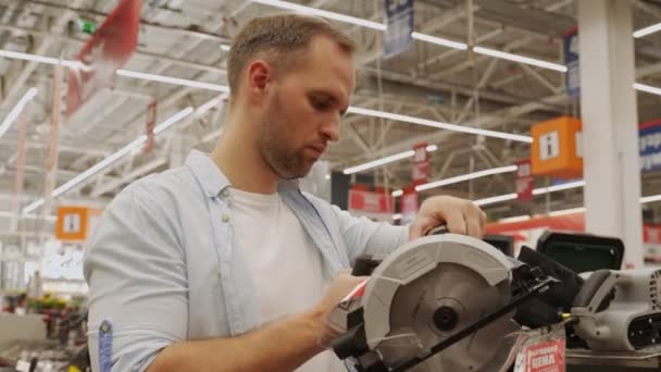 El hombre elige una sierra circular en un taller de herramientas. Male selecciona un producto en una ferretería. — Vídeo de stock