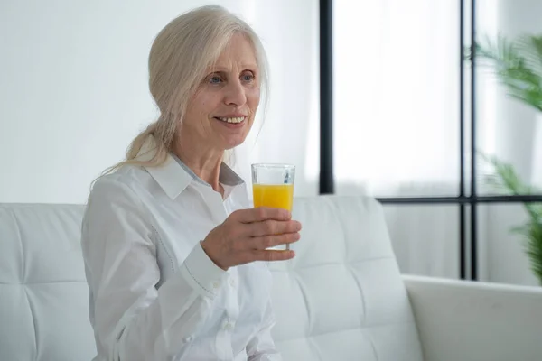 Senior woman drinking orange juice sitting on the couch, Old people retirement and healthy lifestyles — 图库照片