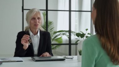 Elderly female real estate agent hands over the keys to an apartment to a female client