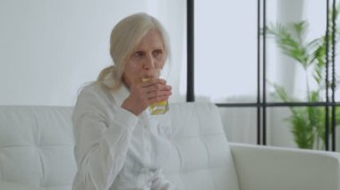Senior woman drinking orange juice sitting on the couch, Old people retirement and healthy lifestyles