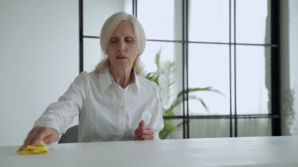 Mature woman wipes a wooden table with a rag. Elderly woman smiling and wipe away dust — Stockvideo