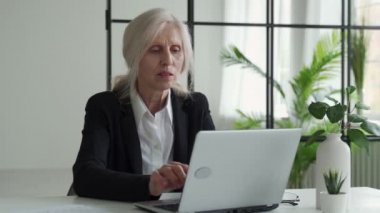 Tired elderly businesswoman, suffering from eye strain, after working on a laptop in the office
