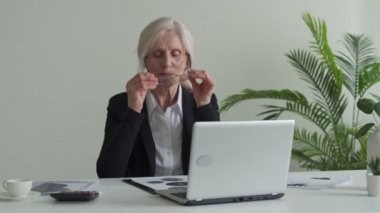 Tired frustrated gray-haired woman, takes off glasses feeling eye strain from computer.