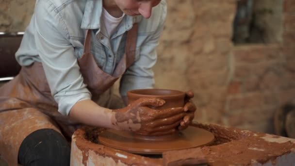 Potter çarkında çalışan çömlekçi kadın kil tenceresi yapıyor. Usta elleriyle kil oluşturuyor atölyede esrar yaratıyor. — Stok video