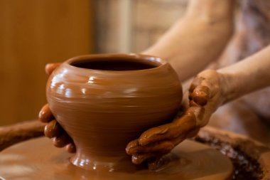 Potter çarkında çalışan yaşlı kadın çömlekçi, kil tenceresi yapıyor. Usta elleriyle kil oluşturuyor atölyede esrar yaratıyor.