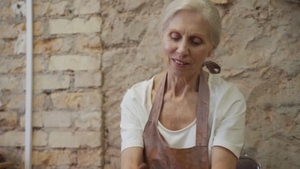 La mujer mayor trabaja con arcilla. Mujer alfarero amasa y humedece la arcilla antes del trabajo — Vídeos de Stock