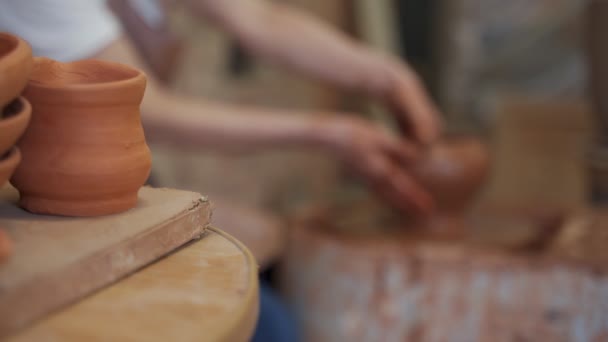 Senioren vrouwelijke handen maken schotels van klei op een pottenbakkerswiel. Aardewerk workshop vrouw is beeldhouwen een kom achter een roterende pottenbakkerswiel — Stockvideo