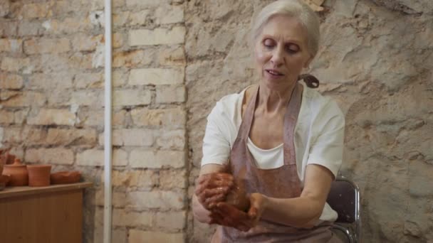 Kıdemli kadın kille çalışıyor. Kadın çömlekçi işten önce kil yoğurur ve nemlendirir. — Stok video