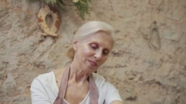 Potter çarkında çalışan yaşlı kadın çömlekçi, kil tenceresi yapıyor. Usta elleriyle kil oluşturuyor atölyede esrar yaratıyor.
