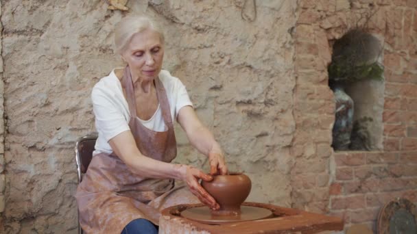 一位穿着围裙的老年女性陶工在陶瓷作坊里做一个壶 — 图库视频影像