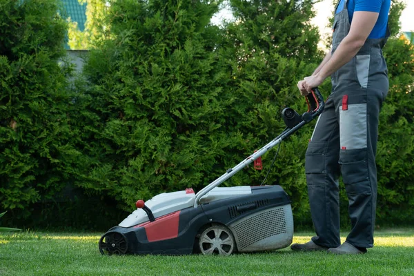 작업복을 입은 젊은 정원사 가 땅에 잔디깎는 기계를 사용 한다 — 스톡 사진