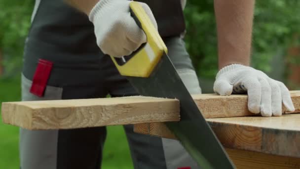 Carpintero hombre sierra una tabla de madera con una sierra de mano. — Vídeo de stock