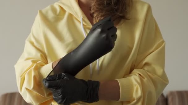Detailní záběr na ruce mladé ženy, jak si nasazuje silné černé lékařské nitrilové rukavice. Ochrana proti virům. — Stock video