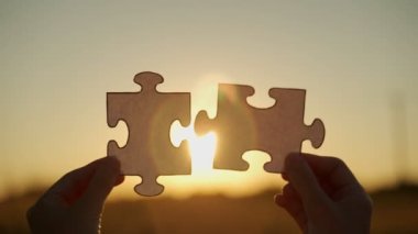 Yeni fikir ve sistem. Kadınların elleri gün batımının arka planında bir yapboz oluşturur.