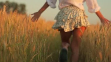 Gün batımında genç güzel bir kadın buğday tarlasında koşar, atlar ve ellerini kaldırır.