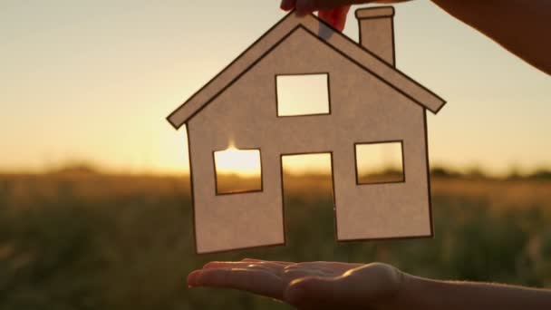 Concept immobilier - gros plan de la silhouette d'une femme au coucher du soleil femme mains tenant maison en papier — Video