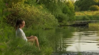 Genç bir kadın rıhtımda oturmuş, göle çıplak bacaklarıyla su sıçratıyor. Kadınların ayakları suya dalarken tazeliği hissederler.