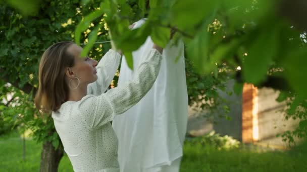 Zeitlupe Seitenansicht einer jungen Frau, die saubere Bettwäsche an einer Wäscheleine an der frischen Luft aufhängt — Stockvideo