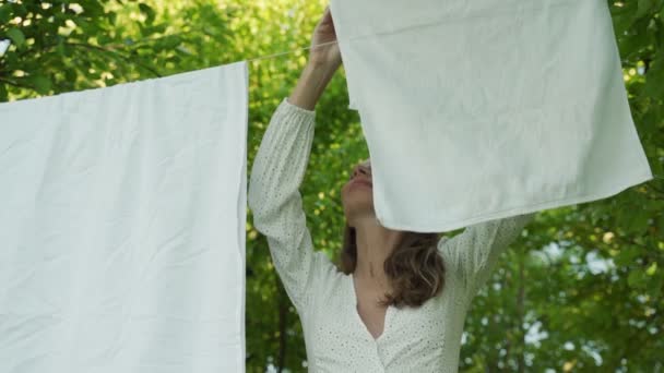 Młoda kobieta wisi czystą bieliznę na sznurze na świeżym powietrzu na tle jabłoni — Wideo stockowe