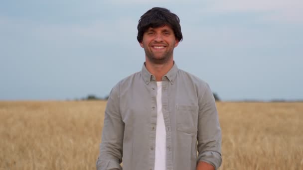 Man boer kruist zijn armen en kijkt naar de camera tegen de achtergrond van een tarweveld — Stockvideo