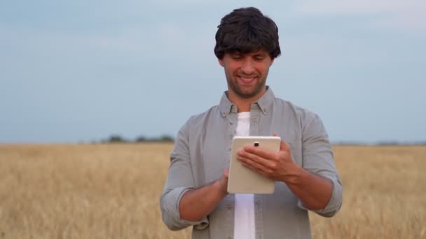 Man farmer using digital tablet computer standing in a wheat field and using apps and checking quality and growth of crops for agriculture — Stockvideo