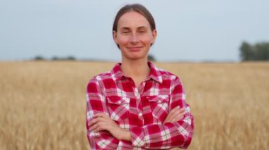 Portrait of a pretty farmer woman with her arms crossed, standing in a wheat field and looking at the camera.