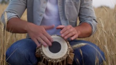 Close-up of a man playing a djembe sitting in a wheat field