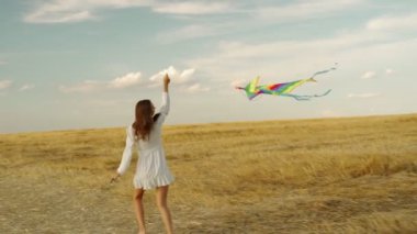 Genç ve güzel bir kız sarı bir alanda çok renkli bir uçurtmayla koşuyor..