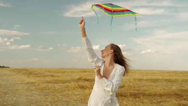 Elbiseli kadın uçurtmayla koşuyor. Kadın gün batımında buğday tarlasına oyuncak bir uçurtma fırlatıyor.. — Stok video