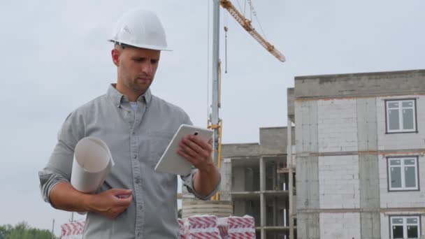 건축 현장에서 백 헬멧을 쓴 남자 기술자가 태블릿 컴퓨터로 카메라를 보며 미소짓는다 — 비디오