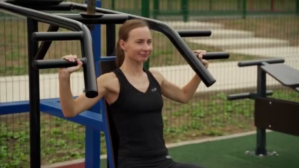 Mladá žena cvičení na rameno lis stroj venku — Stock video