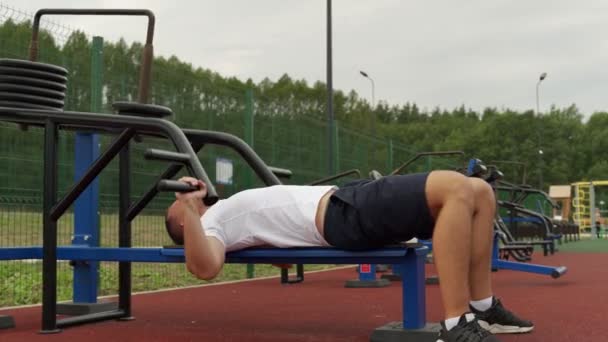 Jonge mannelijke atleet op een simulator traint zijn borstspieren in de buitenlucht. Training van spiergroepen van het bovenlichaam. — Stockvideo