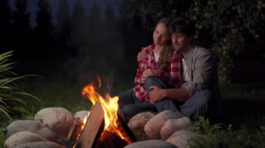 Geceleri kamp ateşinin yanında oturan genç çift.