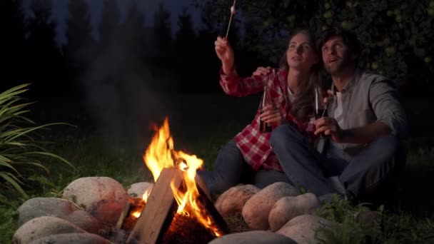Młoda para, mężczyzna i kobieta-podróżnicy, siedzą w pobliżu płonącego ognia, ciesząc się pięknym widokiem na nocne niebo pełne gwiazd — Wideo stockowe