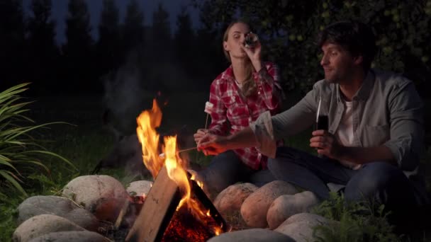 Casal bonito está descansando com um marshmallow perto da fogueira à noite. — Vídeo de Stock