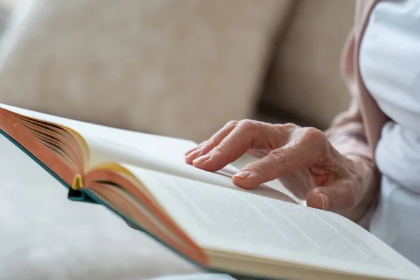 Mulher idosa lendo o livro em casa, close-up. Uma mão de mulher vira uma página em um livro. — Fotografia de Stock