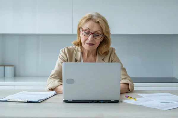 Una anciana sonriente usando un portátil y mirando a la cámara. Una mujer de negocios usa su portátil. — Foto de Stock