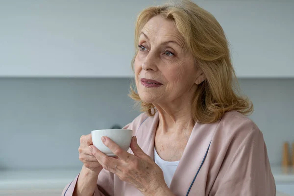 La felicidad de una anciana en un albornoz bebiendo café por la mañana, soñando — Foto de Stock