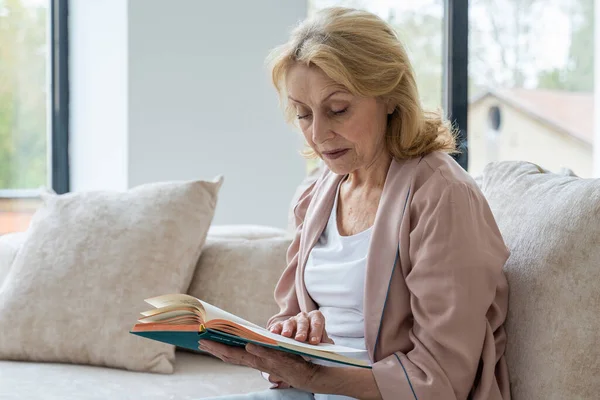 Mujer mayor descansando en la sala de estar. Ella está leyendo novela — Foto de Stock