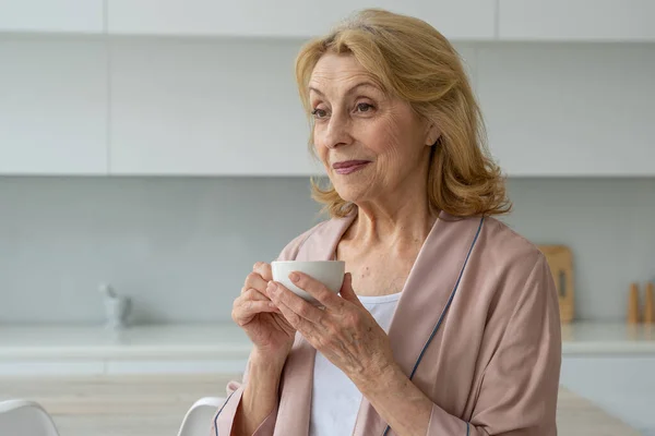 La felicidad de una anciana en un albornoz bebiendo café por la mañana, soñando — Foto de Stock