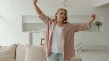 Aktif yaşlı bir kadın evde pilates yapıyor, oturma odasında antrenman yapıyor.