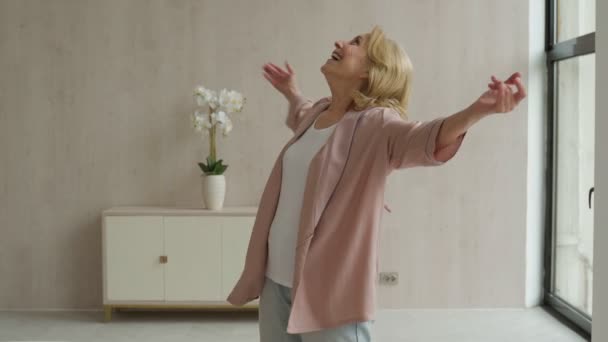 Veselá starší žena poslouchá hudbu a tance ve svém obývacím pokoji — Stock video