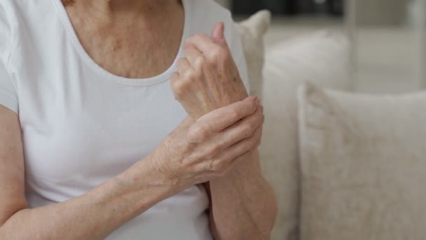 Mujer mayor de cerca que sufre de artritis de las manos sentadas en el sofá. El concepto de salud mental y atención a las personas mayores — Vídeos de Stock