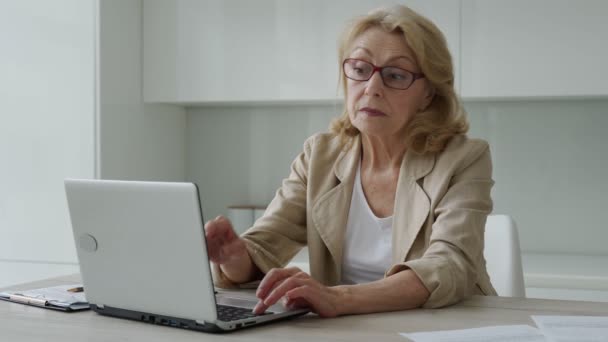 Втомлена розчарована літня жінка, знімає окуляри, відпочиває від роботи на ноутбуці, масажує голову рукою — стокове відео