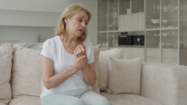 Una anciana que sufre de artritis en las manos sentada en el sofá. El concepto de salud mental y atención a las personas mayores — Vídeo de stock