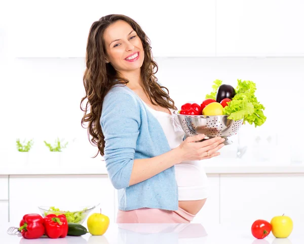 Embarazada joven cocina verduras . Fotos de stock