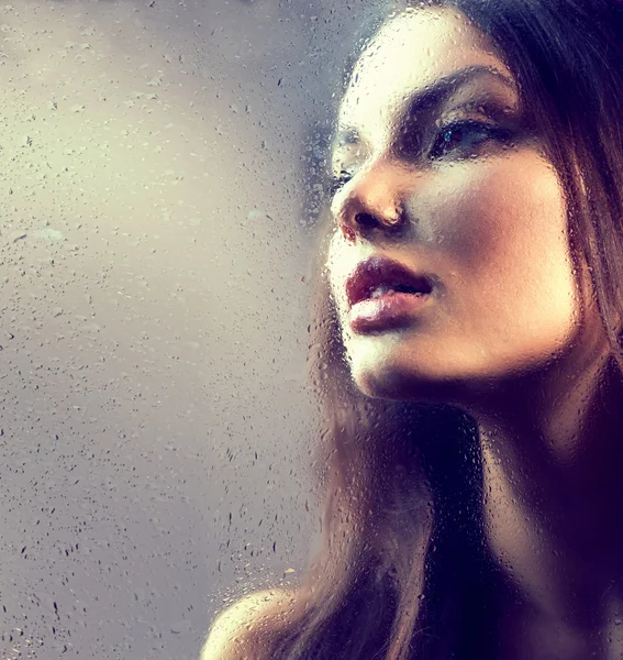 Beauty girl behind  wet glass. Royalty Free Stock Images