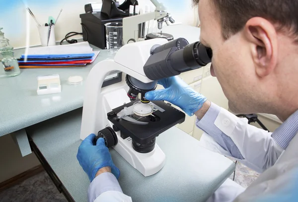 Wetenschapper die door microscoop in laboratorium kijkt — Stockfoto