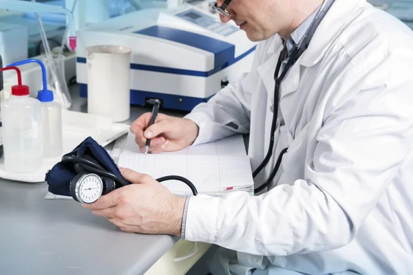 Lekarz stetoskop, okulary i szaty pisać na stole w laboratorium — Zdjęcie stockowe
